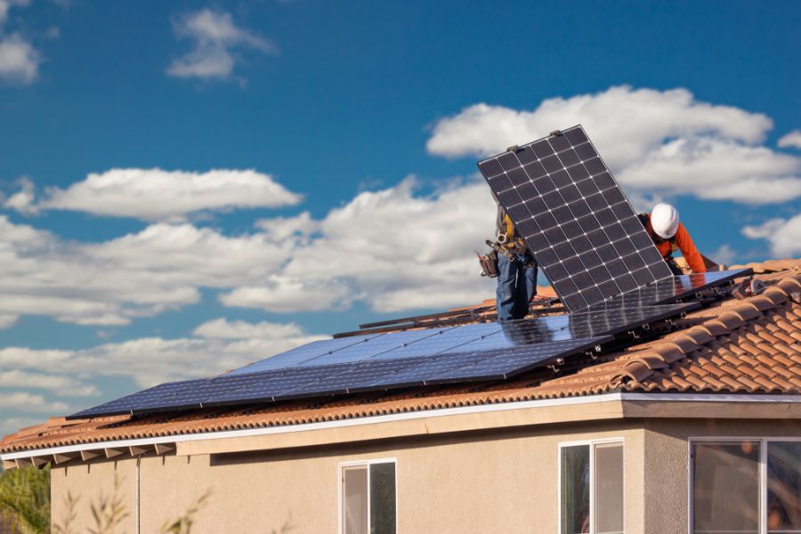 Workers installing solar panels on house roof